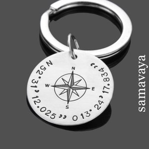 Può includere: Portachiavi in ​​argento con bussola incisa con coordinate e un design a rosa dei venti. Il portachiavi recita "52°31' 2.025 0 13 24 17.834".