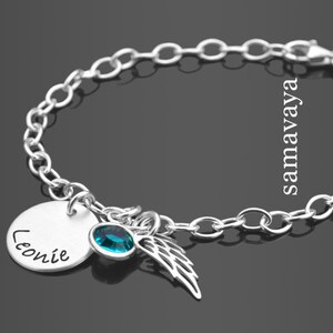 Könnte beinhalten: Silbernes Armband mit einem runden Anhänger, der mit dem Namen "Leonie" graviert ist, einem türkisblauen Kristall und einem silbernen Engelsflügel-Anhänger.