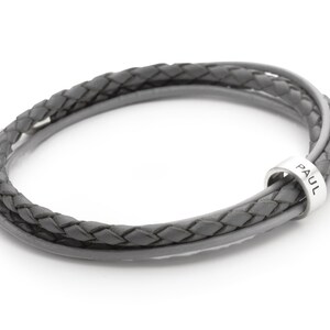 May include: A gray leather bracelet with a silver clasp and a silver bead that says "PAUL".