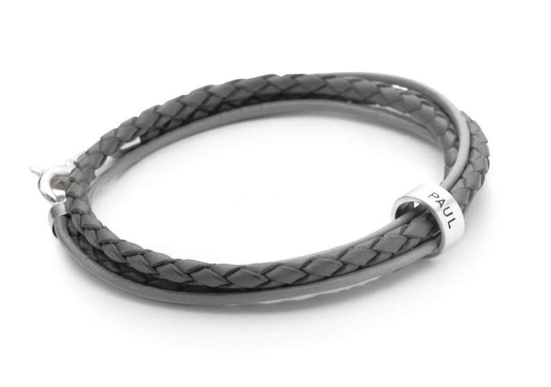 May include: A gray leather bracelet with a silver clasp and a silver bead that says "PAUL".