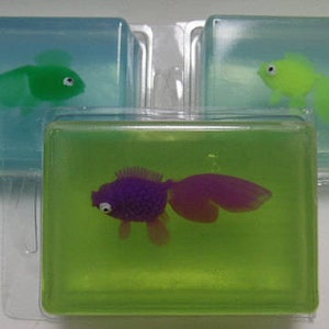 May include: Three clear plastic soap bars with different colored fish inside. The first bar has a green fish, the second bar has a purple fish, and the third bar has a yellow fish.