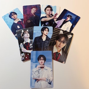 May include: A collection of rectangular photo cards featuring various individuals in different poses. The cards display a range of outfits and backgrounds, with some featuring props like microphones and bunny ear headbands. The color palette includes blues, reds, and blacks.