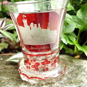 Puede incluir: Una copa de vidrio transparente con base roja y un diseño grabado en blanco de un castillo con el texto "Stolzenfels".