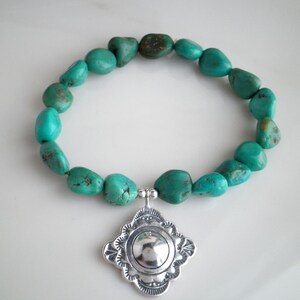 May include: Turquoise stone bracelet with a silver charm in the shape of a four-pointed star. The charm has a round, silver center.