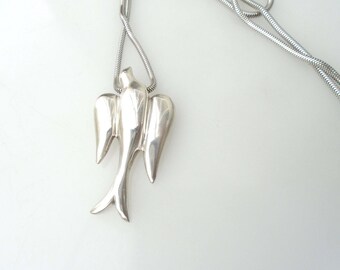 May include: A silver-toned necklace featuring a pendant shaped like a bird in flight with outstretched wings. The pendant is attached to a flexible, rounded snake chain. The entire piece has a smooth, polished, and reflective metallic finish.