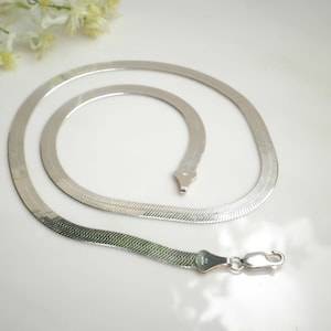 May include: A silver herringbone chain necklace with a lobster clasp.