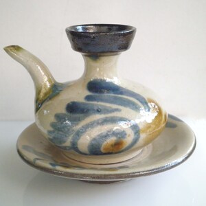 May include: A white ceramic sake set with a blue and brown swirl design. The set includes a small pitcher with a spout and a matching saucer.