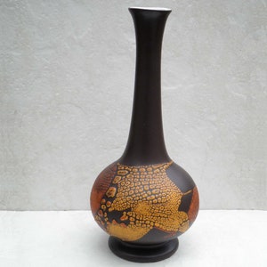 May include: A brown ceramic vase with a bulbous base and a long, slender neck. The vase is decorated with a geometric pattern in shades of orange and yellow.