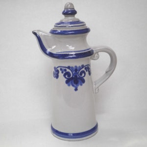Puede incluir: Una jarra de cerámica blanca con un diseño floral azul y blanco y una tapa. La jarra tiene un pico y una asa.