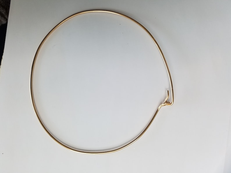 K&ouml;nnte beinhalten: Ein goldfarbener Metallring mit einem Verschluss. Der Ring ist rund und scheint aus d&uuml;nnem Draht zu sein.