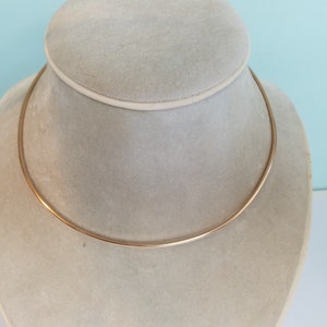 K&ouml;nnte beinhalten: Eine einfache goldene Choker-Kette auf einem wei&szlig;en Pr&auml;sentationsst&auml;nder.