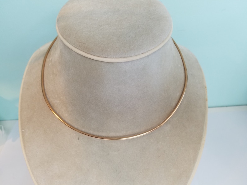 K&ouml;nnte beinhalten: Eine einfache goldene Choker-Kette auf einem wei&szlig;en Pr&auml;sentationsst&auml;nder.