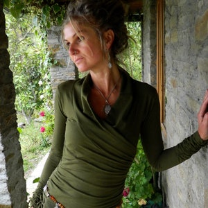 May include: A woman wearing a green long-sleeved shirt with a draped neckline and a silver necklace. She is wearing a belt with silver and orange accents.