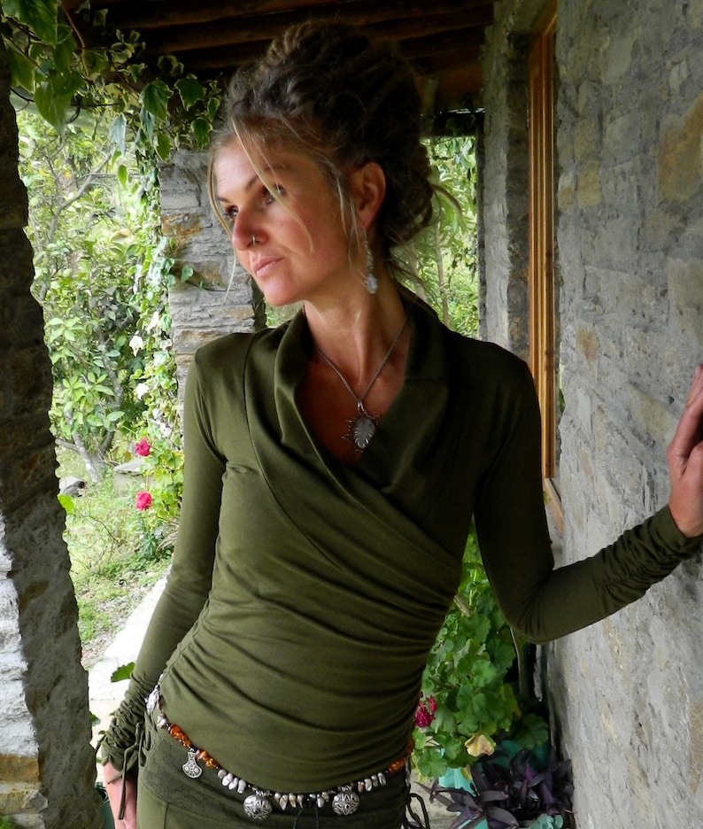 May include: A woman wearing a green long-sleeved shirt with a draped neckline and a silver necklace. She is wearing a belt with silver and orange accents.