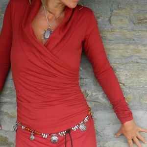 May include: A red long-sleeved wrap dress with a silver pendant necklace and a silver and orange beaded belt.