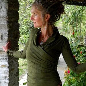 May include: A woman wearing a green long-sleeved shirt with a draped neckline and a silver necklace. She is wearing a beaded belt with silver charms and has dreadlocks.