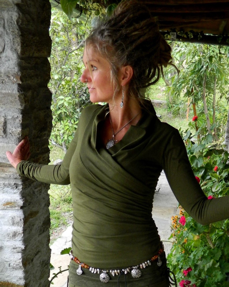 May include: A woman wearing a green long-sleeved shirt with a draped neckline and a silver necklace. She is wearing a beaded belt with silver charms and has dreadlocks.