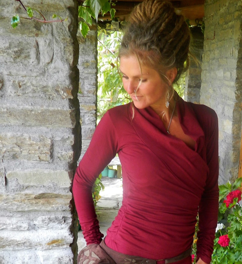 May include: A woman with dreadlocks wears a maroon long-sleeved shirt with a cowl neck. The shirt is made of a soft, stretchy fabric and has a relaxed fit.