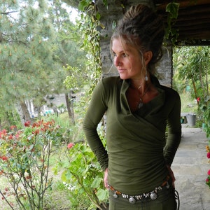 May include: A woman with dreadlocks wears a green long-sleeved shirt with a cowl neck. She is wearing a silver and amber beaded belt.