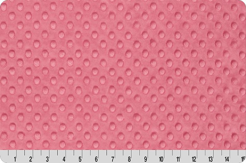 May include: Pink minky fabric with a raised dot pattern. The fabric is shown with a ruler along the bottom, with markings in inches. The fabric is a solid color and has a soft, plush texture.