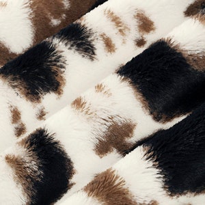 May include: Close-up of a white, brown, and black faux fur fabric with a cowhide pattern.