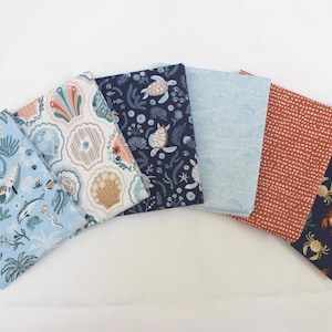 May include: Six folded fabric squares arranged in a fan shape. Patterns include light blue with sea life, white with colorful seashells, dark blue with sea turtles, light blue with wave lines, rust orange with white dots, and dark blue with crabs.