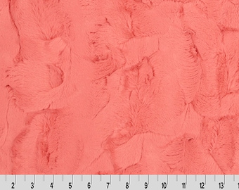 May include: A close-up of a coral-colored faux fur fabric. The fabric has a soft, plush texture and a subtle swirl pattern.