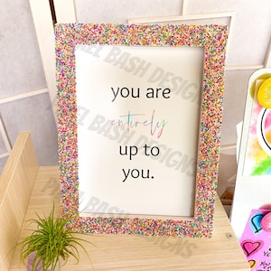 May include: A white picture frame with a colorful sprinkle border. The frame contains a motivational quote that reads "You are entirely up to you."