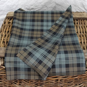 May include: A folded piece of fabric with a blue, brown and black tartan pattern. The fabric is folded in half and the edges are visible.