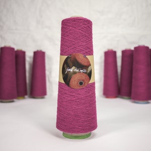 Könnte beinhalten: Eine Spule pinkfarbenes Garn mit einem braunen Etikett, auf dem "from the mills" in weißer Schrift steht.