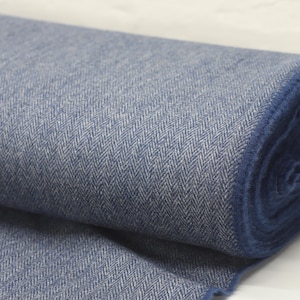 May include: A roll of blue and white herringbone fabric. The fabric is tightly woven with a distinct diagonal pattern. The roll is partially unraveled, revealing the texture and color variations of the material. The fabric appears to be a medium weight, suitable for various sewing projects.
