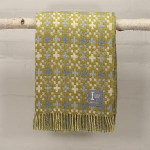 May include: A green and blue woven throw blanket with a geometric pattern. The blanket has a fringe border and a small label that reads "Loom & Bohemian" and "woven with love".
