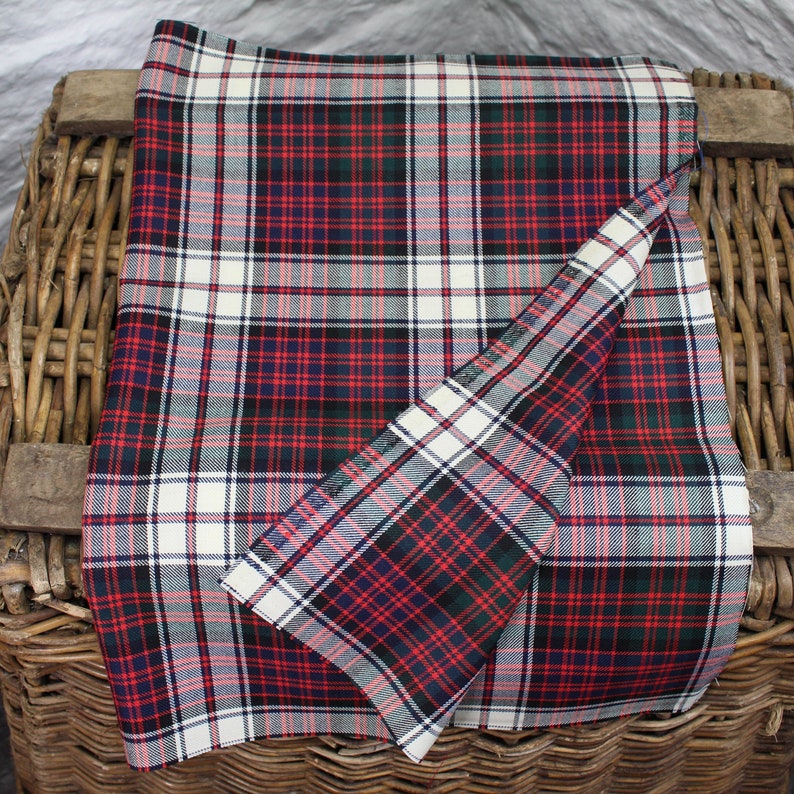 Puede incluir: Una tela tart&aacute;n roja, blanca, verde y azul con un patr&oacute;n de cuadros. La tela est&aacute; doblada por la mitad y est&aacute; sobre una cesta de mimbre.