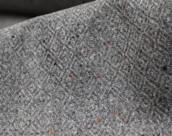 May include: Close-up of a gray tweed fabric with flecks of orange and green. The fabric has a subtle herringbone pattern.