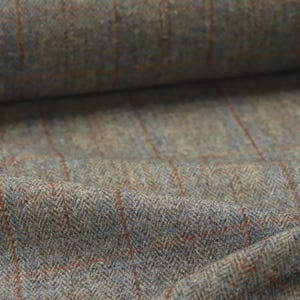 May include: Close-up of a textured fabric with a herringbone weave. The fabric is primarily a muted gray-green color, with thin blue and red lines forming a plaid pattern. The fabric is folded, showing the texture and depth of the material.