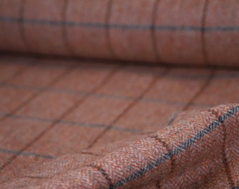 May include: Close-up of a soft, orange and gray plaid fabric with a herringbone weave. The fabric is folded and draped, showing the texture and pattern.