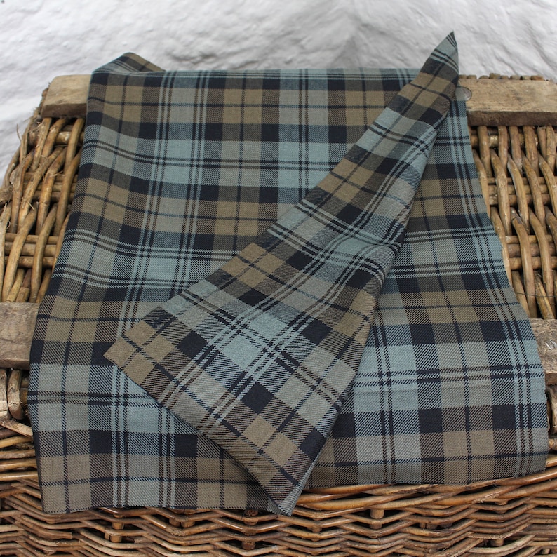 May include: A folded piece of fabric with a blue, brown and black tartan pattern. The fabric is folded in half and the edges are visible.