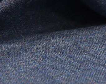 May include: Close-up of a textured fabric in shades of blue and tan. The material has a woven appearance, with a mix of light and dark threads creating a mottled effect. The fabric is folded, revealing shadows and depth.