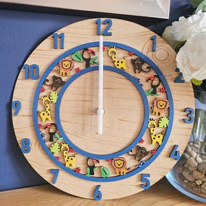 May include: A wooden clock with a blue rim and animal illustrations. The clock face has numbers 1 through 12 and a white hand. The animals include giraffes, toucans, monkeys, and lions.