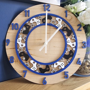 May include: A wooden clock with a blue and white design featuring video game controllers and stars. The clock face has black numbers and white hands.