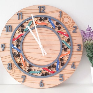 May include: A wooden clock with a gray circle around the numbers. The numbers are gray and the clock hands are white. The clock face has a design of colorful cars and stars around the circle.