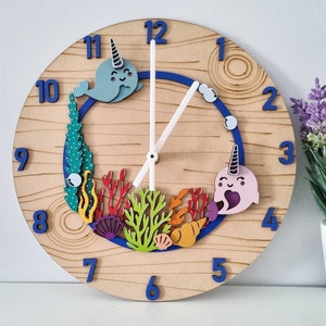 May include: A wooden clock with a blue and white design featuring narwhals and coral. The clock face has Roman numerals and a blue and white hand.