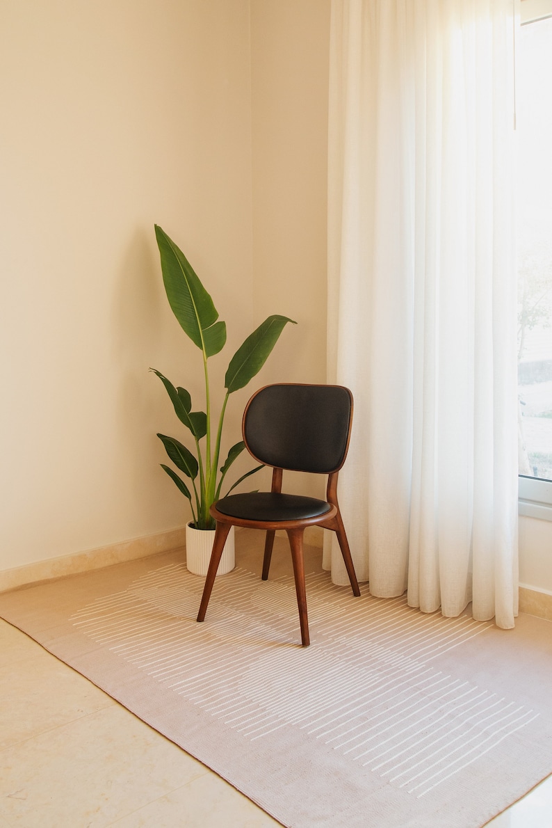 May include: A black leather chair with wooden legs sits on a beige rug with white stripes. A potted green plant is in the corner of the room.