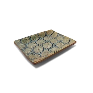 Peut inclure: Plateau de service rectangulaire en céramique avec un motif de feuilles. Le plateau a un bord marron clair et un motif de feuilles bleu et beige. Les feuilles sont soulignées en marron plus foncé et sont disposées en motif répété. Le fond est bleu moucheté.