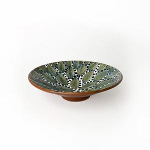 Può includere: Una ciotola in ceramica con un motivo a foglie verdi e blu. La ciotola ha una base rialzata ed è decorata con punti bianchi.