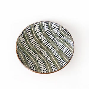 May include: A white ceramic plate with a wavy pattern of green and black dots. The plate has a brown rim.