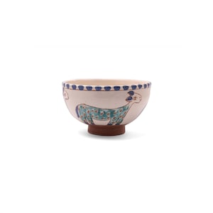 Peut inclure: Un bol en céramique avec un extérieur crème, orné d'un motif peint à la main d'un animal bleu et vert. Le bord est décoré de points bleus, et le bol repose sur une base marron. Ce bol décoratif est idéal pour servir des aliments.