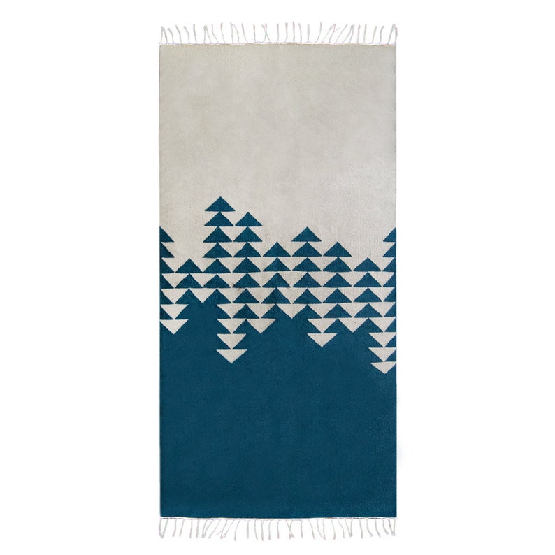 Op de afbeelding: Een blauw en wit geometrisch tapijt met een franje rand. Het tapijt heeft een witte achtergrond met een blauw geometrisch patroon van driehoeken.