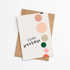 Multicoloured modern Christmas card with bauble illustrations and 'Seasons Greetings' message. Card is lying on top of Kraft brown envelope.