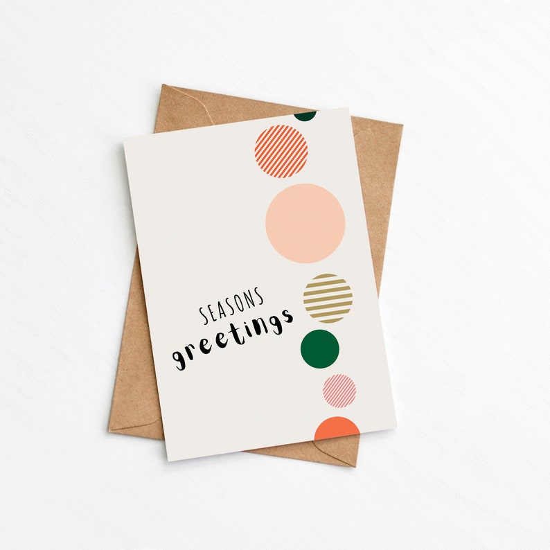 Multicoloured modern Christmas card with bauble illustrations and 'Seasons Greetings' message. Card is lying on top of Kraft brown envelope.